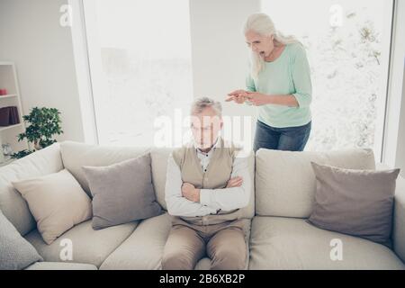 Foto eines gereizten gealterten Mannes, der auf Divan sitzt und den Vorwürfen einer skandalösen aggressiven Dame lauscht, die seine Defekte und Charakterfehler zählt Stockfoto