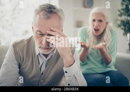 Nahaufnahme des aufgebrachten traurigen, erschöpften Mannes, der den Kopf berührt und Kopfschmerzen von der Stimme seiner aggressiven Frau hat Stockfoto