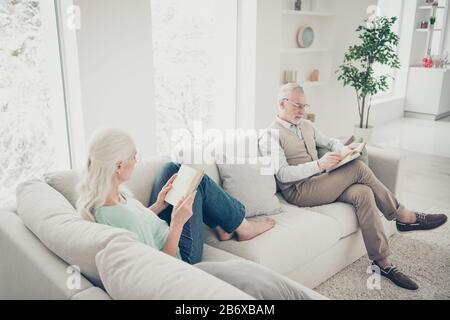 Oben über dem Winkel Foto von lieblichen Ehepartnern Lesen Sie gedrucktes Buch mit Denim Jeans Teal braune Pullover Brillen sitzen auf Divan im Zimmer Stockfoto
