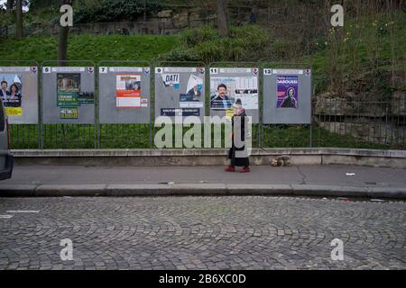 Frau geht an den Anzeigetafeln vorbei, in denen Wahlkandidaten bei französischen Kommunalwahlen, rue Ronsard, Montmartre, 75018 Paris, Frankreich, März 2020, angezeigt werden Stockfoto