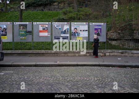 Woman Walks by Panels, in denen Wahlkandidaten bei französischen Kommunalwahlen, rue Ronsard, Montmartre, 75018 Paris, Frankreich, März 2020, angezeigt werden Stockfoto