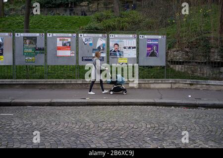 Frau mit Kinderwagen geht an Panels vorbei, in denen Wahlkandidaten bei französischen Kommunalwahlen, rue Ronsard, Montmartre, 75018 Paris, Frankreich, März 2020, angezeigt werden Stockfoto