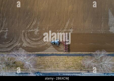 Antenne Blick von oben auf einen Traktor, Mähdrescher pflügen landwirtschaftliche Flächen im Frühjahr Stockfoto