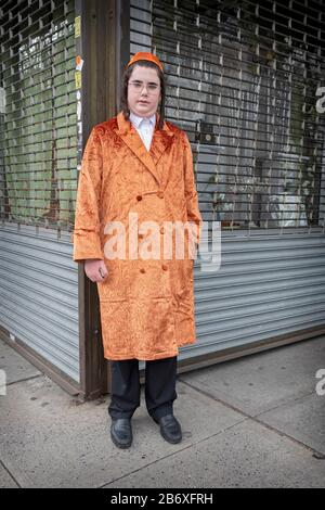 Ein junger Satmar jüdischer Schüler in seinem orangefarbenen Purim-Kostüm sammelt wohltätige Zwecke für seine Schule. In Williamsburg, Brooklyn, New York City. Stockfoto