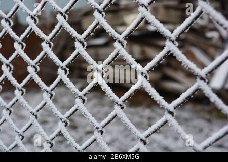 Metallisches altes rostiges Netz aus Nischen, mit weißem Schnee, hellem Hochfrost und schönen Schneeflocken dekoriert. Stockfoto