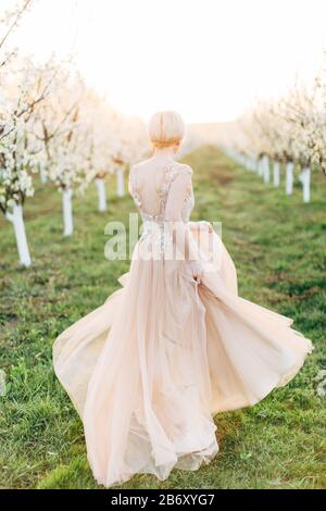 Junge schöne romantische blonde Kaukasusfrau in langen, leichten, eleganten Kleidspazieren und laufen im blühenden Garten, Rückansicht Volllingenporträt Stockfoto