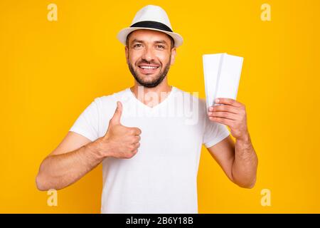 Porträt seines hübsch aussehenden attraktiven fröhlichen fröhlichen Kerls mit weißem T-Shirt, das in Handtickets hält, die einen Hinweis auf die Anzeige von Thumbup anzeigen Stockfoto