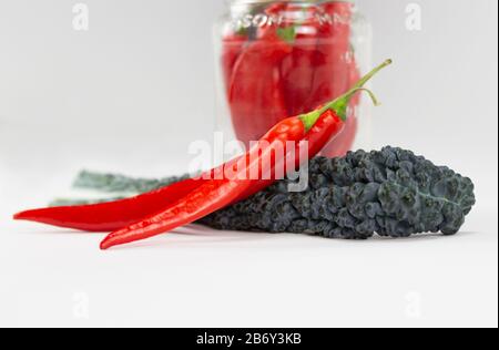 Anordnung der roten Chilischoten und eines lacinato-kalischen Blattes auf weißem Bakkgrund, auch Dinosaurier-Kale, flacher Kale, toskanischer Kale oder italienischer Kale genannt Stockfoto