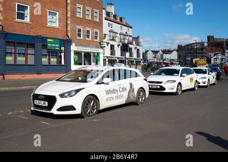 Taxistand mit weißen Taxis in New Quay Straße Whitby, North Yorkshire England Großbritannien warten Stockfoto