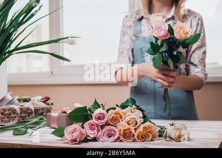 Hände junger Blumenhändler, die mit frischen Blumen arbeiten, die einen Blumenstrauß aus rosa Rosen auf dem Tisch machen. Nahaufnahme. Stockfoto