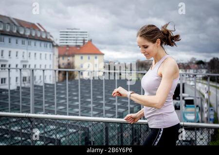 Junge Sportlerin luft über eine Brücke in der Stadt und überprüft dort auch die Smartwatch. Die junge Sportlerin läuft über eine Brücke in der Stadt. Stockfoto