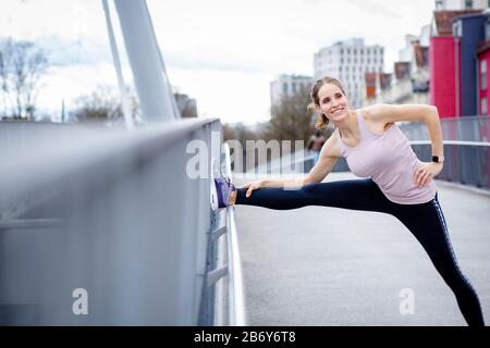 Junge Sportlerin macht Dehnungen nach dem Sport in der Stadt. Junge Sportlerin macht nach dem Sport in der Stadt Dehnübungen. Stockfoto