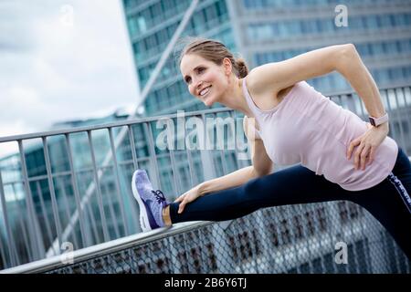 Junge Sportlerin macht Dehnungen nach dem Sport in der Stadt. Junge Sportlerin macht nach dem Sport in der Stadt Dehnübungen. Stockfoto