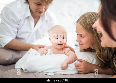 Schöne lächelnde junge Familie Mutter Papa ältere Tochter und neugeborenes Baby liegen auf einem großen Bett in einem hellen Schlafzimmer. Konzept der freundlichen kaukasischen Fam Stockfoto
