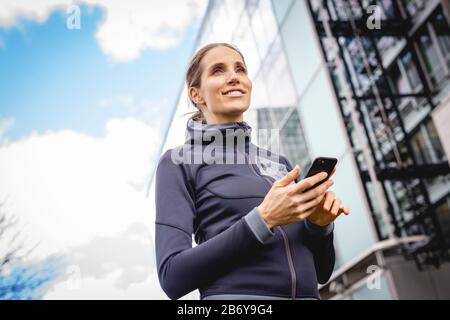 Junge, sportliche Frau macht dem Joggens eine Pause mit griffiger Hand. Junge, sportliche Frau macht sich eine Pause mit einem Handy in der Hand. Stockfoto