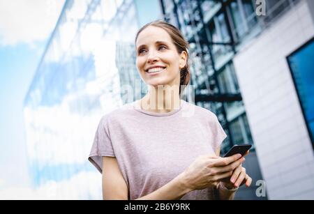 Junge, sportliche Frau macht dem Joggens eine Pause mit griffiger Hand. Junge, sportliche Frau macht sich eine Pause mit einem Handy in der Hand. Stockfoto