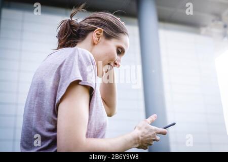 Junge, sportliche Frau macht dem Joggens eine Pause mit griffiger Hand. Junge, sportliche Frau macht sich eine Pause mit einem Handy in der Hand. Stockfoto