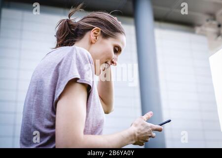 Junge, sportliche Frau macht dem Joggens eine Pause mit griffiger Hand. Junge, sportliche Frau macht sich eine Pause mit einem Handy in der Hand. Stockfoto