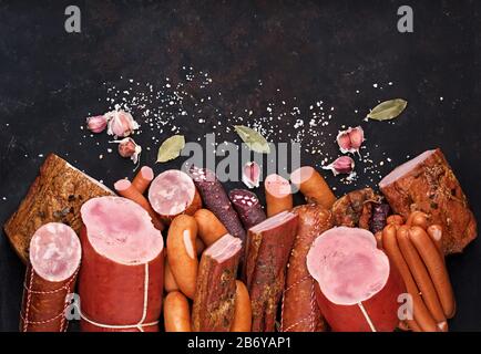 Eine Auswahl an Fleischprodukten, darunter Wurstschinken, Speck, Gewürze Knoblauch auf schwarzem Hintergrund von oben. Gekochtes Ham Meatworks Produktfoto. Stockfoto