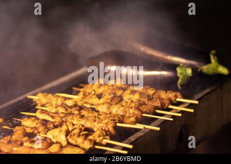 Hühnerbrocken Spieße, Grill, Grill. Auf einem Grillplatz aus Metall. In den Grillphasen. In der Nähe der gerösteten Aubergine. Dunkler Nachthintergrund, koscheres Essen. Viele sm Stockfoto