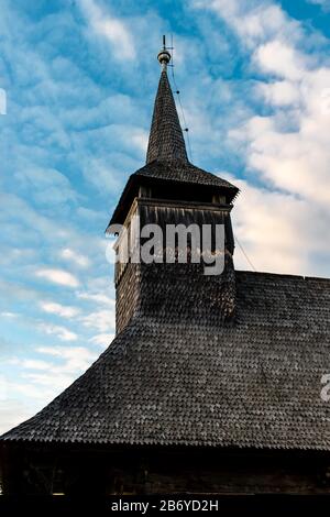Blick nach oben auf den Kirchturm einer alten Holzkirche an einem wolkigen blauen Sonnenuntergangshimmel in Maramures Stockfoto