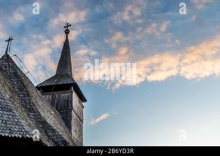 Blick nach oben auf den Kirchturm einer alten Holzkirche an einem wolkigen blauen Sonnenuntergangshimmel in Maramures Stockfoto