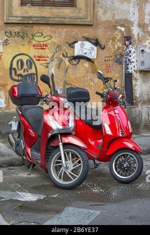 FLORENZ ITALIEN ROTES MOTORRAD UND ROTER VESPA-ROLLER VOR EINER WAND MIT GRAFFITI-KUNST Stockfoto