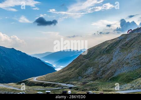 Bergrettungshaus oben auf dem Berg mit Autos, die auf kurvenreicher Straße am Grund fahren und nebelige, waldbedeckte Berge im Hintergrund Stockfoto