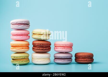 Makkaroni-Kekse verschiedener Farben sind in Form von Pyramidenstufen auf blauem Grund angeordnet. Freier Speicherplatz. Das Konzept des Minimalismus Stockfoto