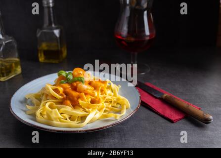 Frische Tagliatelle mit Garnelen und Diabolosoße auf einer hellen Platte mit einem Glas Wein. Stockfoto