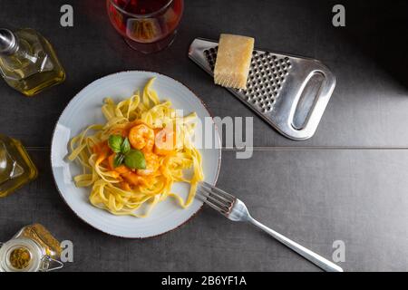 Frische Tagliatelle mit Garnelen und Diabolosoße auf einer hellen Platte mit einem Glas Wein. Draufsicht. Stockfoto