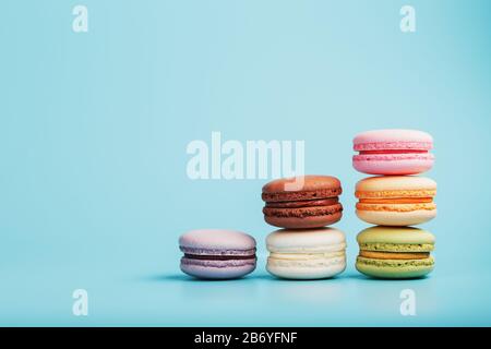 Makkaroni-Kekse verschiedener Farben sind in Form von Pyramidenstufen auf blauem Grund angeordnet. Freier Speicherplatz. Das Konzept des Minimalismus Stockfoto