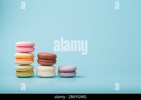 Makkaroni-Kekse verschiedener Farben sind in Form von Pyramidenstufen auf blauem Grund angeordnet. Freier Speicherplatz. Das Konzept des Minimalismus Stockfoto