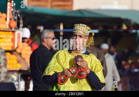 Ein Gnaoua/Gnawa-Musiker, der Krakebs/Qarkabebs spielt, marokkanische Castinets, während er Touristen in Jemaa el-Fnaa in Marrakeschs Medina unterhält Stockfoto