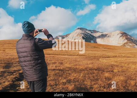 Touristen fotografieren Berge, die mit Wolken bedeckt sind, auf einem Smartphone. Ein Reisender nimmt Fotos und Videos von erstaunlicher Natur auf digitalen Medien auf. Adv Stockfoto