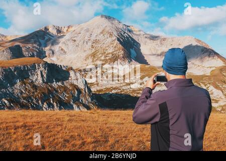 Touristen fotografieren Berge, die mit Wolken bedeckt sind, auf einem Smartphone. Ein Reisender nimmt Fotos und Videos von erstaunlicher Natur auf digitalen Medien auf. Adv Stockfoto