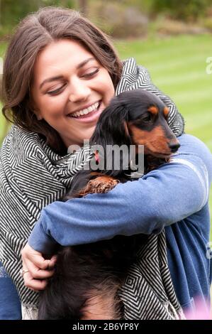 Fröhliche junge Frau, die ihren kleinen langhaarigen Dachsund kuschelt Stockfoto