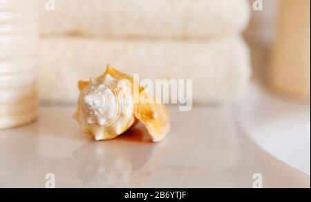 Сockleshell und Bad weiße Baumwollhandtücher, Keramikflasche auf verschwommenem Badezimmer-Innenhintergrund mit Waschbecken und Hahn. Stockfoto