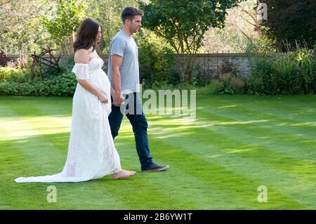 Schöne schwangere junge Frau, die an einem schönen Sommertag Hand in Hand mit ihrem Partner geht Stockfoto