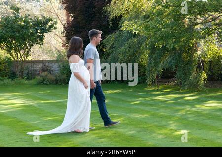 Schöne schwangere junge Frau, die an einem schönen Sommertag Hand in Hand mit ihrem Partner geht Stockfoto