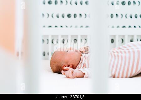Seitenansicht eines neugeborenen Mädchens, das in ihrer modernen Krippe liegt Stockfoto