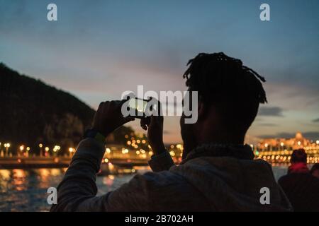 Afrikanischer Mann, der bei Nacht in Budapest ein Bild von einem Boot aufgenommen hat Stockfoto