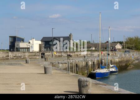 Ein heller sonniger Frühlingstag am Steinkai im Carlingford Harbour mit zwei blau-weißen Yachten, die an der Quayside mit Carlingford Yacht Club links gebunden sind. Stockfoto