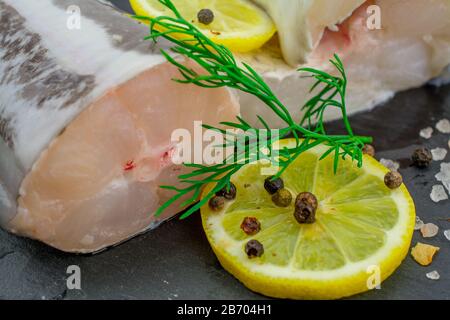 Frische Fischfilets aus Kongeraal, Zitronenkräuter, Pfeffer, Salz auf schwarzem Grund Stockfoto