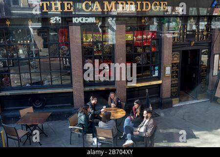 Eine Gruppe von Freunden genießen Getränke, während sie außerhalb Von Cambridge sitzen, einem typischen Pub im Cambridge Circus im Londoner West End am 12. März 2020, in London, England. Das Cambridge wurde im Jahr 1887 an der Stelle Der King's Arms neben dem Palace Theatre erbaut. Stockfoto