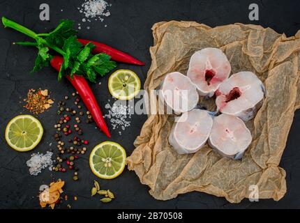 Frische Fischfilets aus Kongeraal, Zitronenkräuter, Pfeffer, Salz auf schwarzem Grund Stockfoto