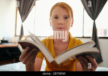 Young Redhead Girl Studieren Und Zeigen Book To Camera Stockfoto