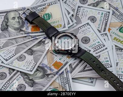 Armbanduhr liegt auf dem Hintergrund verstreuter US-Dollar Stockfoto