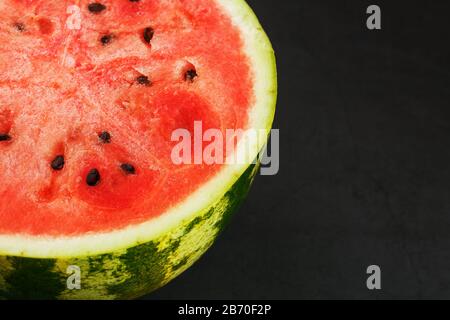 Die Hälfte der leckeren und reifen roten Wassermelone auf schwarzem Grund, die Struktur des saftigen Fruchtfleischs der reifen roten Wassermelone mit Samen Stockfoto