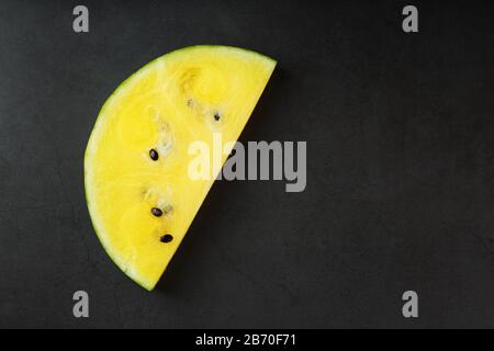 Saftige Scheibe gelber Wassermelone auf steinschwarzem Grund. Konzeptionelle Farben des Sommers. Draufsicht als Hintergrund oder Substrat Stockfoto